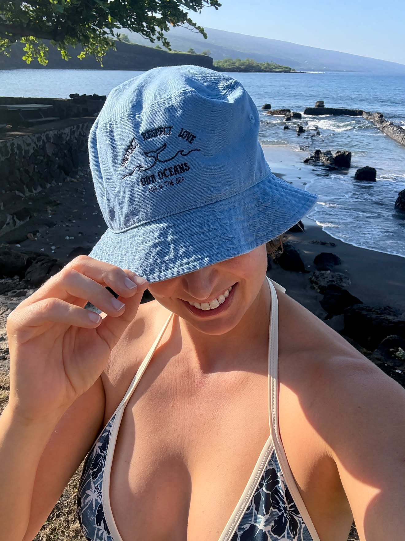 Woman on a rocky beach wearing the organic cotton Ocean Bucket Hat in slate blue