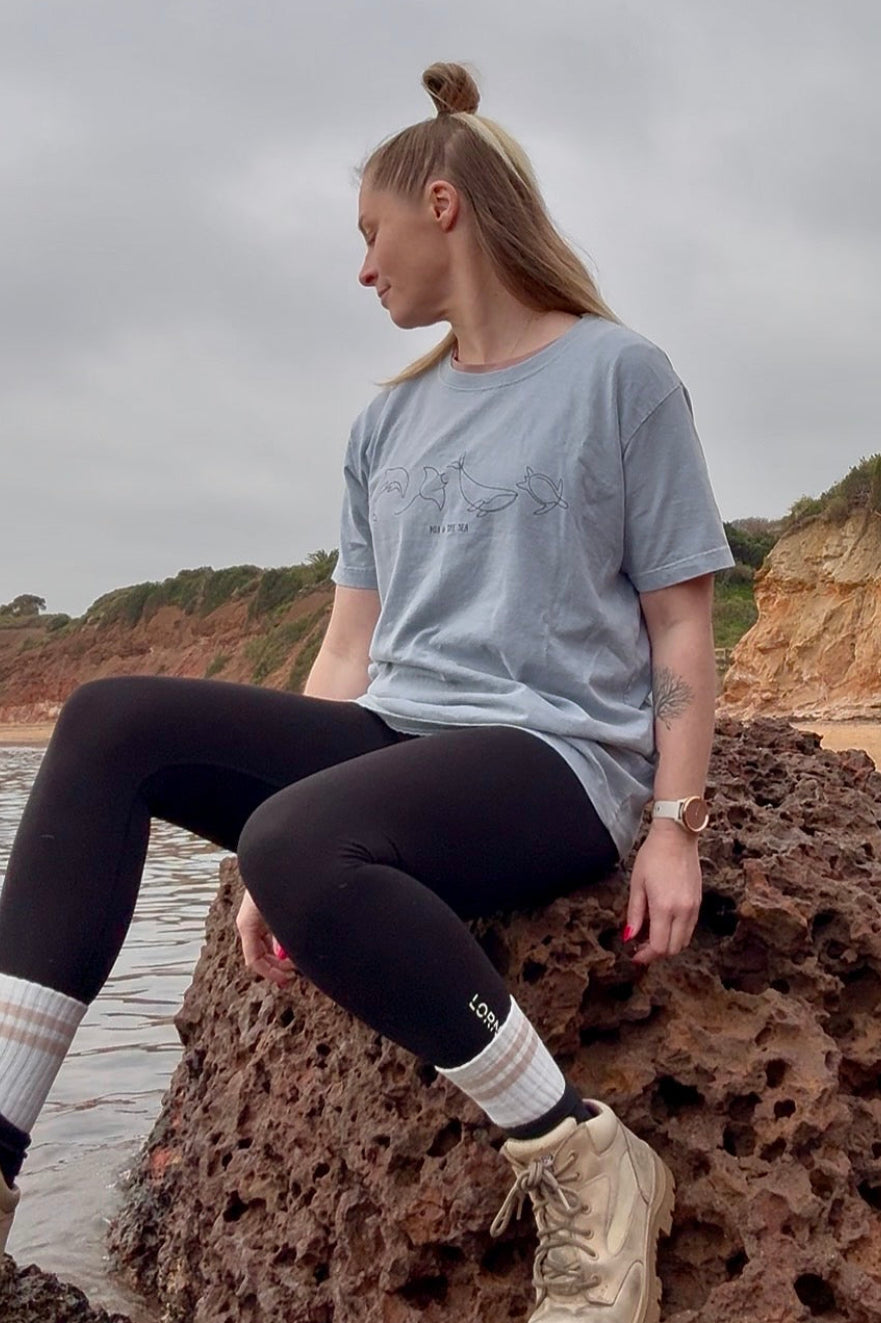 Woman sitting on a rock  by the ocean wearing the light washed denim marine life t-shirt